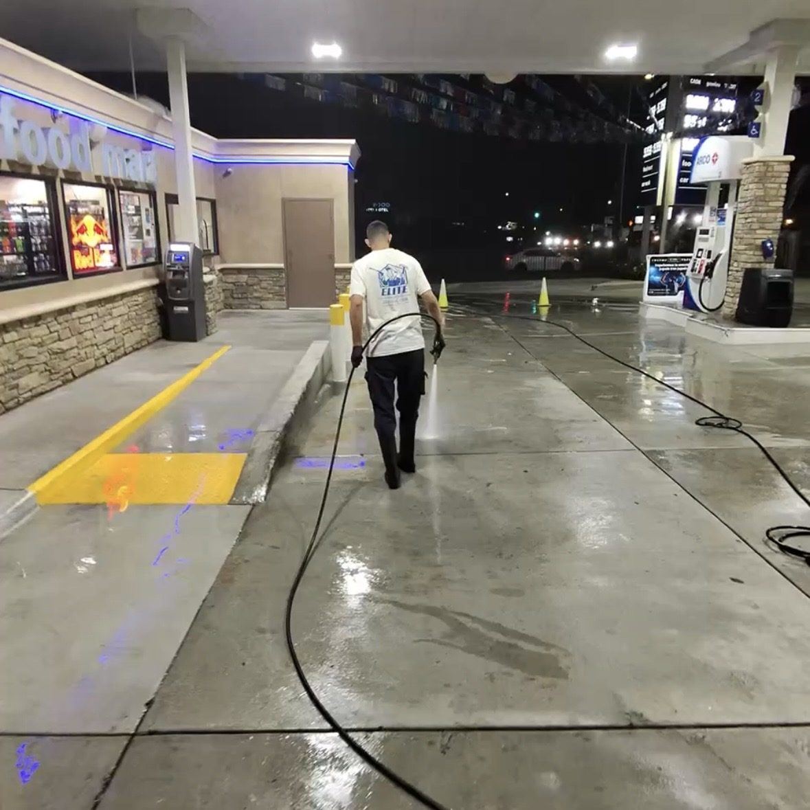 Elite technician pressure washing a commercial gas station and convenience store lot at night