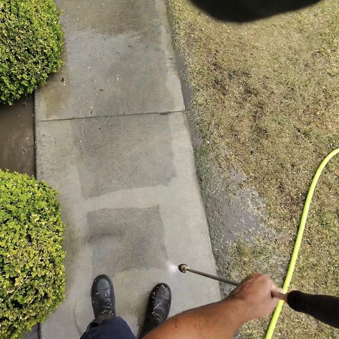 Pressure washing a concrete sidewalk along a landscaped lawn