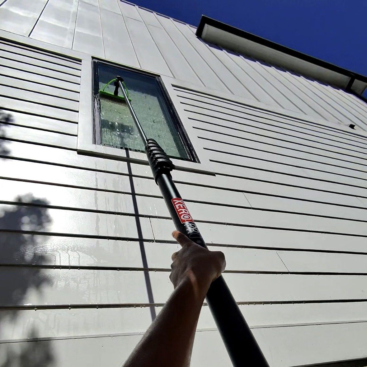 Elite Home Exterior Maintenance technician squeegee cleaning a window